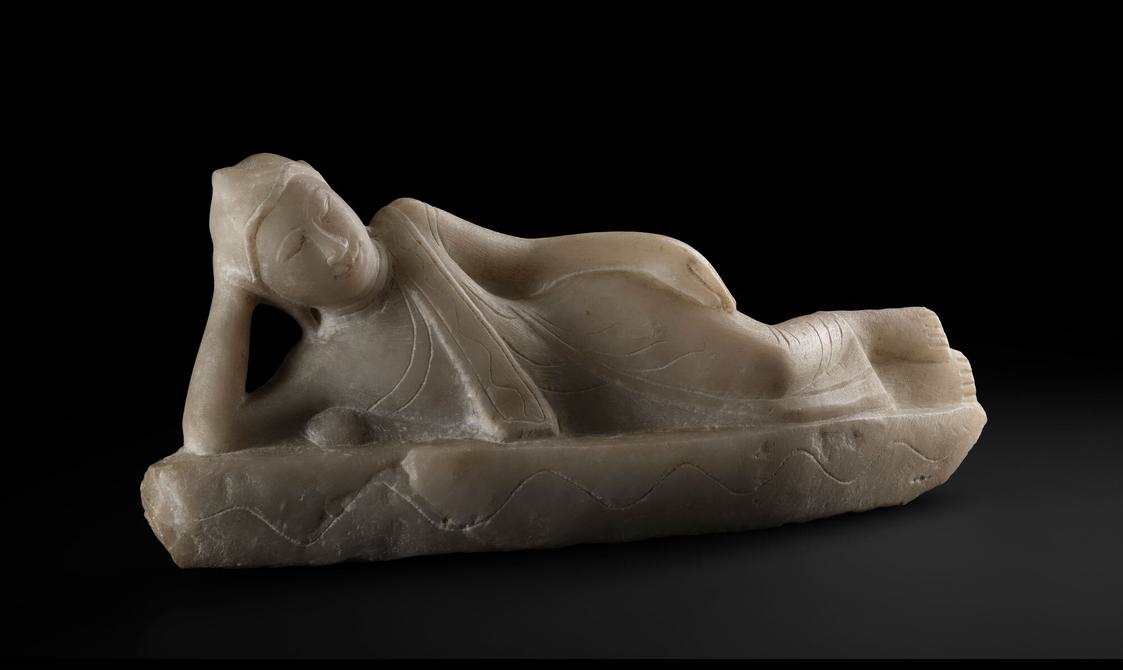 Photograph of an alabaster sculpture of a Buddha figure lying on its side.