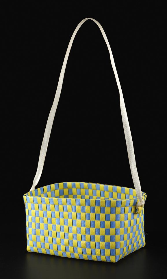 A rectangular basket woven in alternating strips of yellow and blue plastic. It has a long strap handle attached to the top.