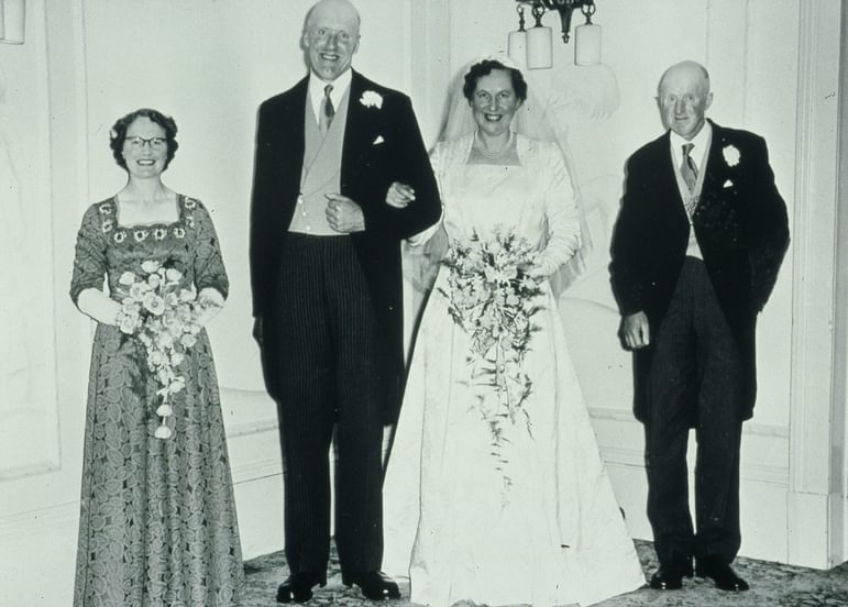 A black and white wedding photograph of the bride and groom with a man and woman standing either side of them.