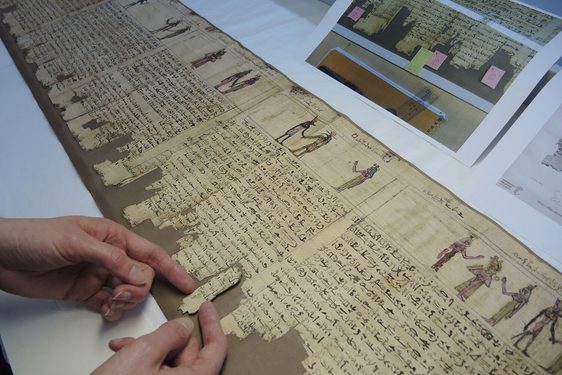 A pair of hands placing a fragment of an ancient Egpytian scroll