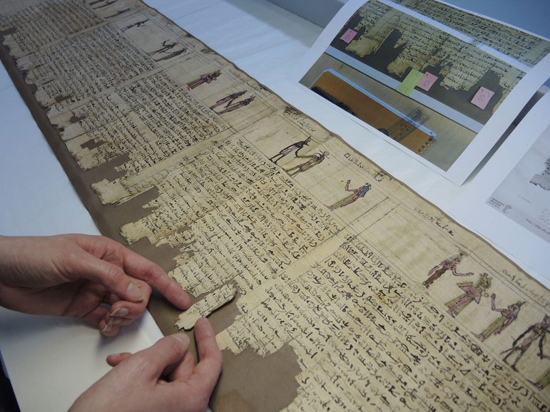 A pair of hands placing a fragment of an ancient Egpytian scroll