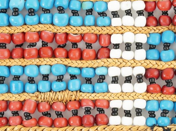 close-up of beadwork with a pattern of red and blue horizontal stripes and one white vertical crossing them all.