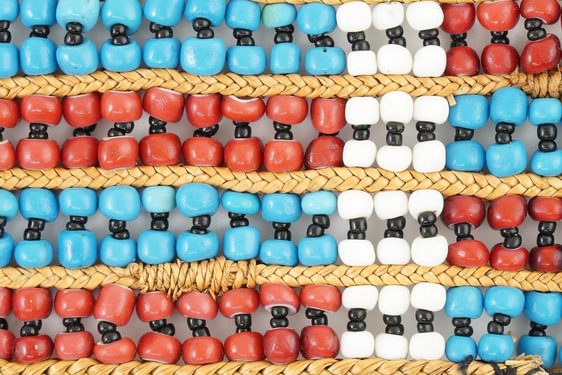 close-up of beadwork with a pattern of red and blue horizontal stripes and one white vertical crossing them all.