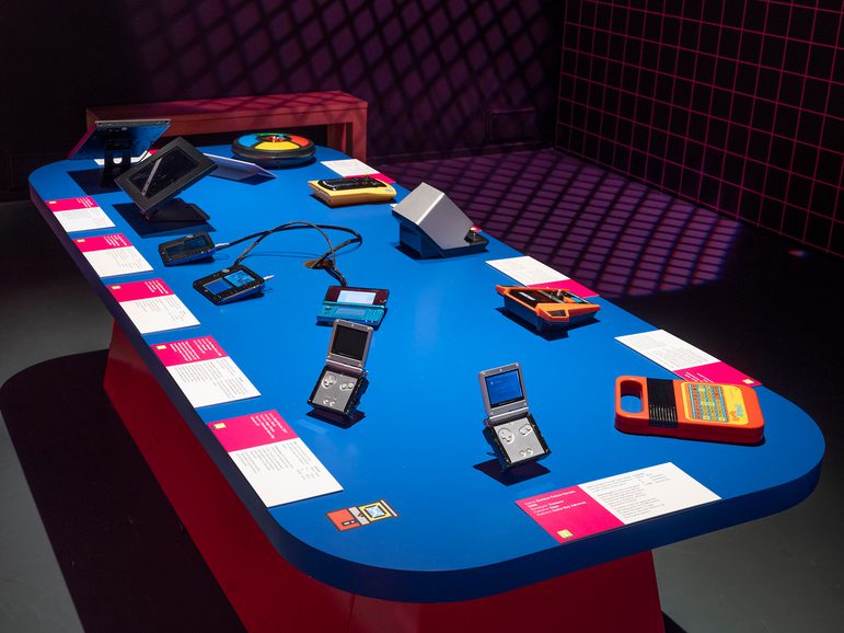 A blue table in the Game On exhibition. Each place is set with a different handheld console.