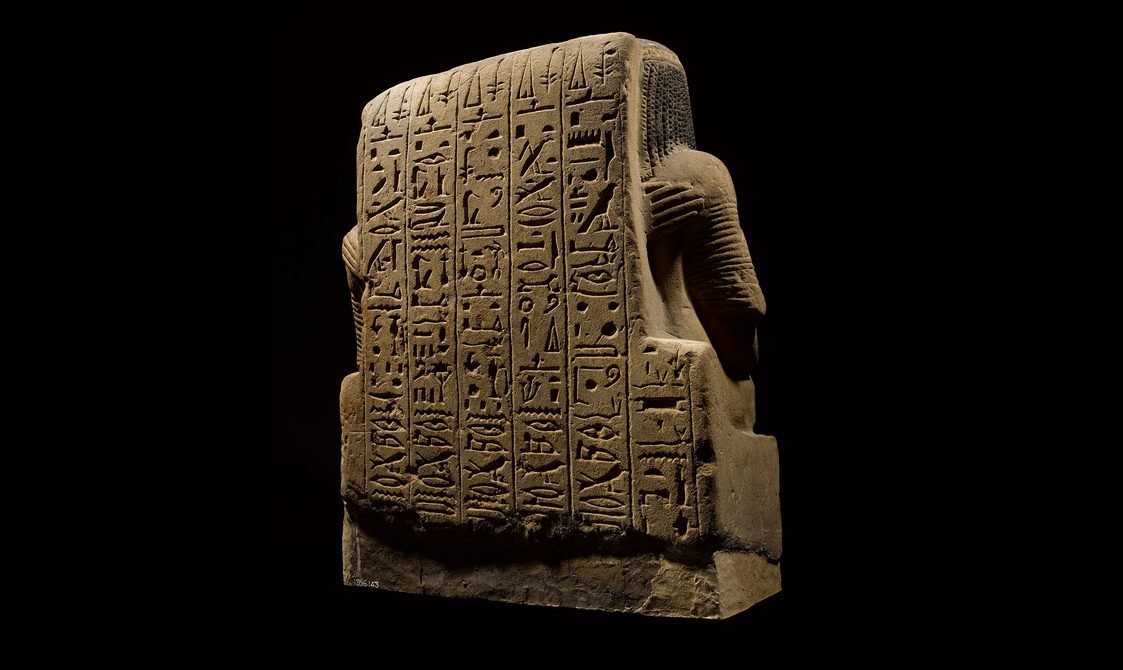 The back of an Egyptian statue of a seated man and woman, with a panel covered in hieroglyphic text.