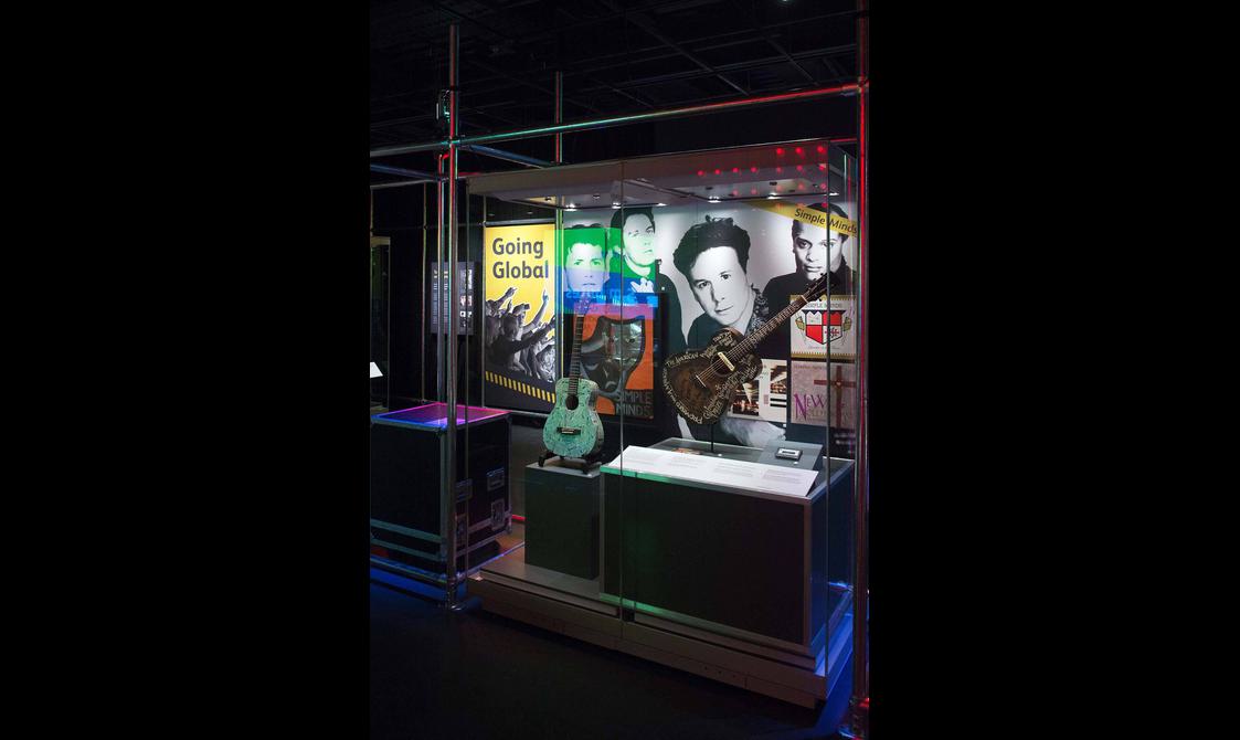 Two acoustic guitars that belonged to the band Simple Minds on display in a museum exhibition.