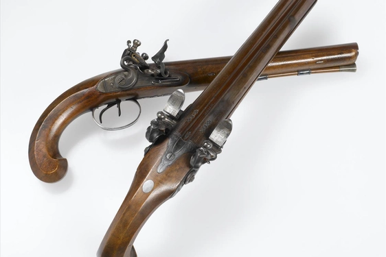 Two wood and metal pistols set against a white background. One pistol is laid on a side and the other placed on top.