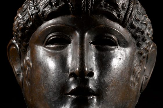 A bronze Roman face mask of a young female face.