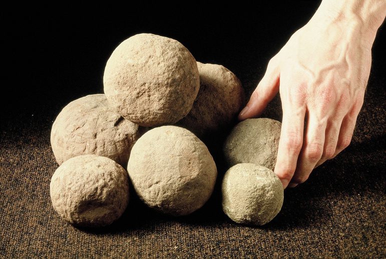 A pile of seven or eight stone balls with a person's hand for scale. Most are the size of a clenched fist.