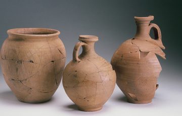 Three jugs side by side, all light brown. On left is the widest one with no lid, while other two are slimmer with handles.