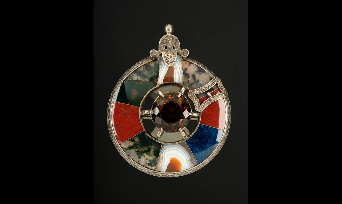 A round brooch with colourful sections of polished agates. A faceted yellow cairngorm is set in the centre