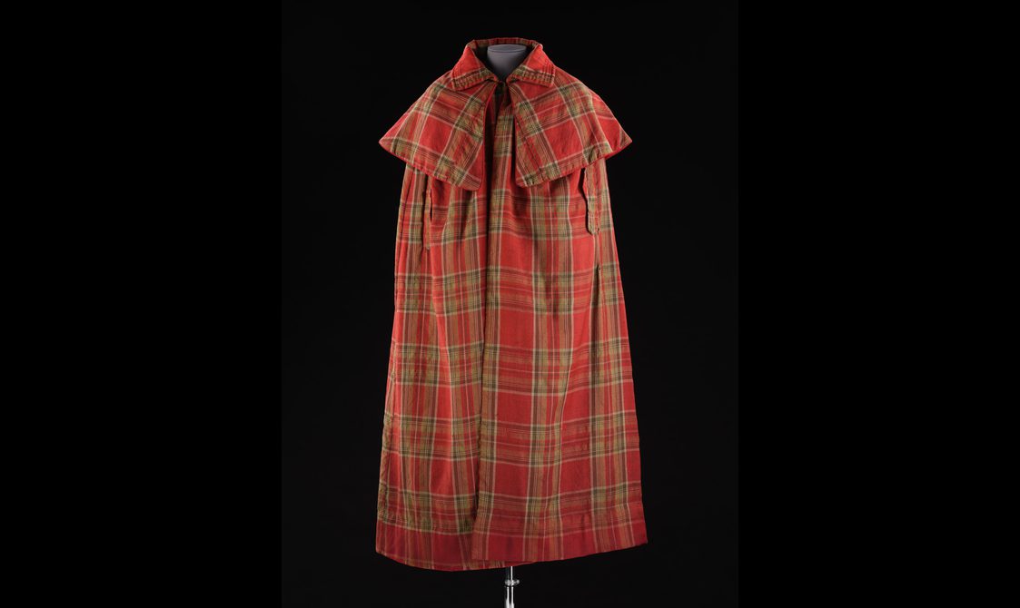 A mannequin wearing a long red tartan cloak with a large collar