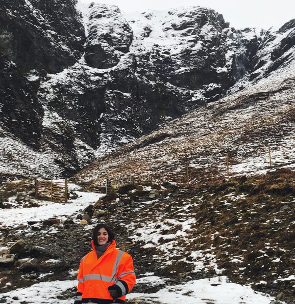 A snowy mountain landscape with a person dressed in orange high vis gear in the foreground.