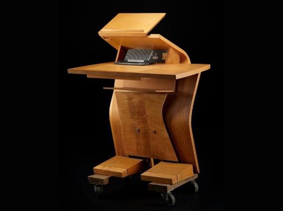 Light brown wooden desk shaped like a humanoid robot, with two blocky 'feet', a tall, curved centre, and two flat surfaces at the top.