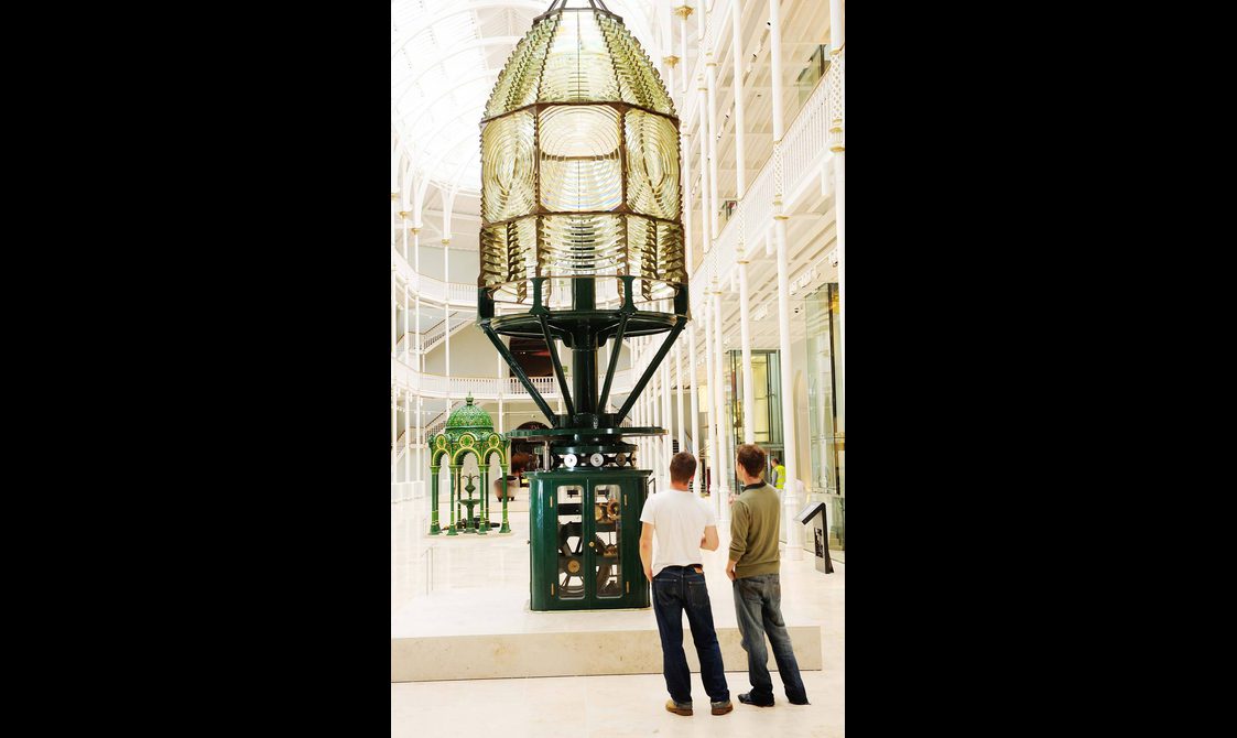 Two visitors looking at a lighthouse in the Grand Gallery of the National Museum of Scotland.