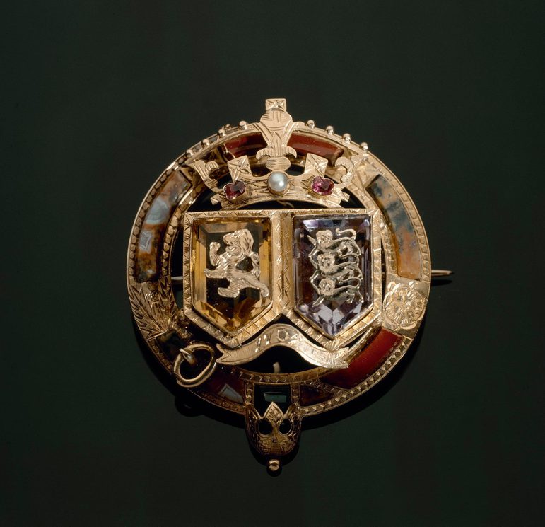Round gold brooch set with pebbles. Two shields with lions topped by a crown.