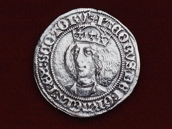 Silver coin, set against red background,with embossed writing to the edge of the coin that centers a bust portrait of a man with shoulder length hair, wearing a crown.