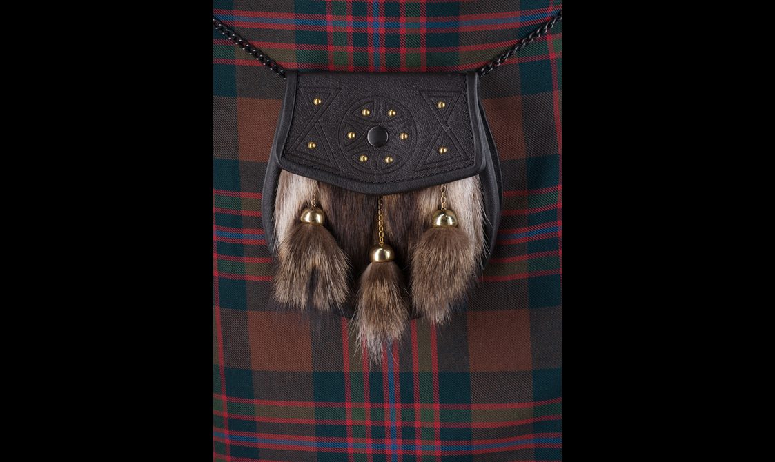 A sporran decorated with animal skin hanging from a red tartan kilt.
