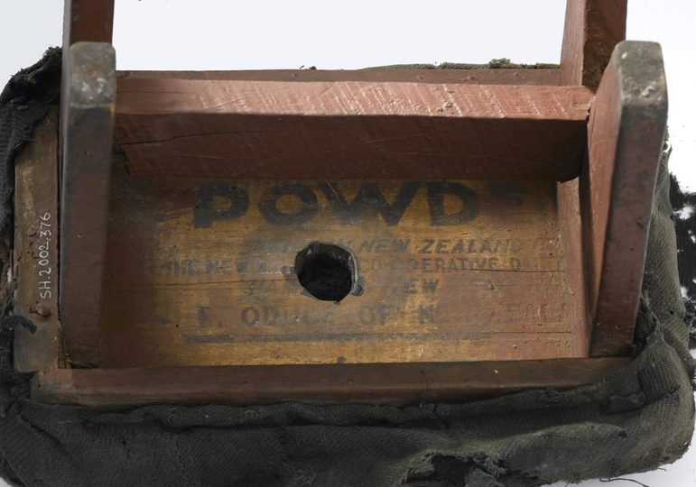 Closeup of the underside of a tiny wooden stool, where the painted words 'POWDER', 'New Zealand', and 'Product of' are visible.