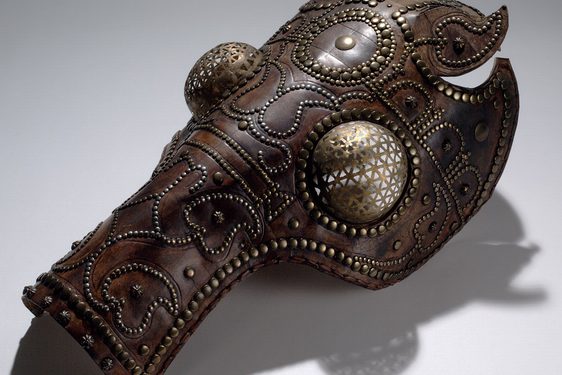 Reddish-brown leather helmet shaped like a horse's head. Its eyes are guarded with metal spheres resembling a fly's eyes.