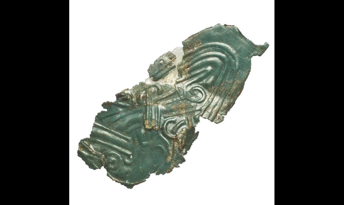 A piece of bronze that has turned green with Celtic markings on it