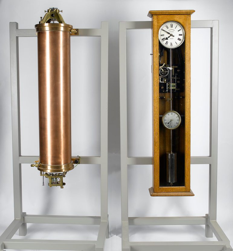 A tall copper cylinder on the left, and a tall wooden clock with the face at the top and a long pendulum hanging the length of the box on the right.