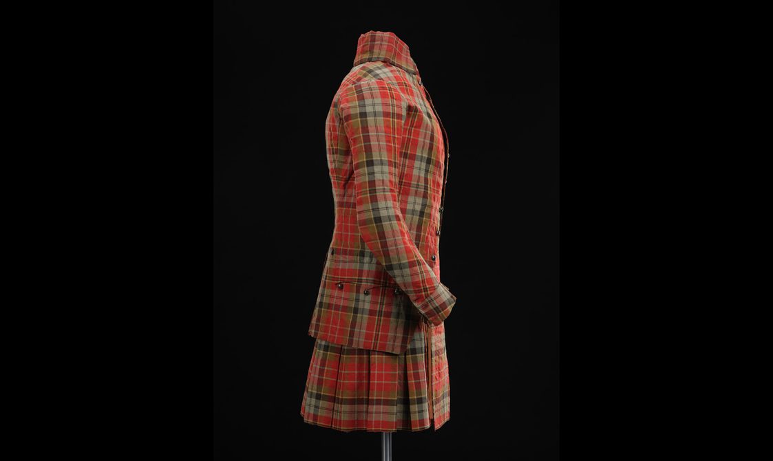 Side view of mannequin wearing a red tartan kilt with matching jacket.