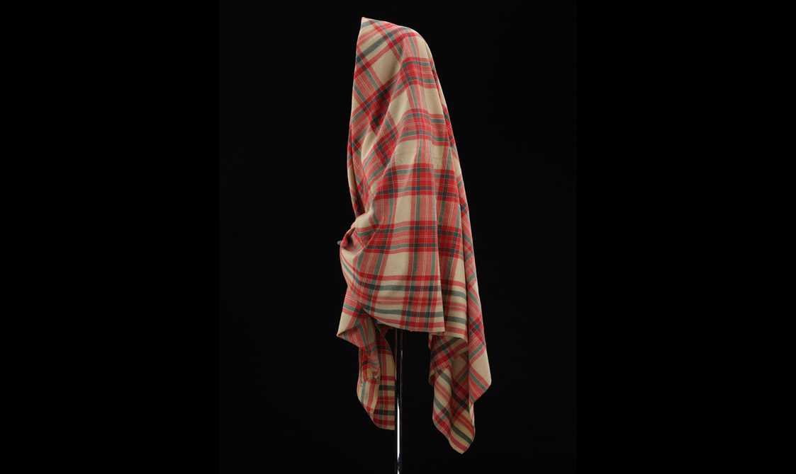 Side view of a mannequin wearing a red and cream tartan shawl.
