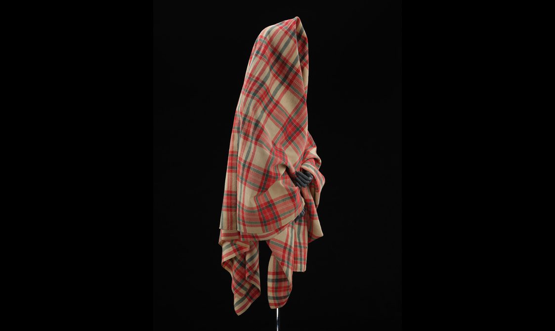 Side view of a mannequin wearing a red and cream tartan shawl.