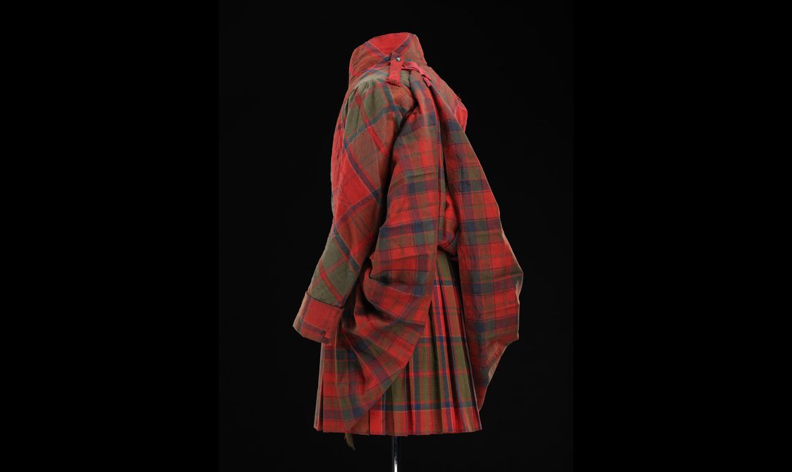 Side view of a mannequin wearing a red tartan kilt with matching jacket and pinned jacket tails.