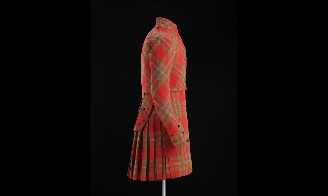 Side view of a mannequin wearing a red tartan kilt with matching jacket.