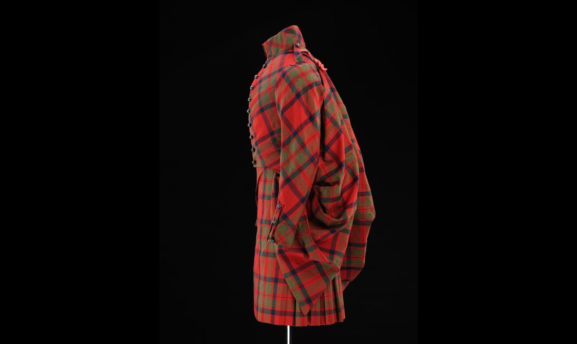 Side view of a mannequin wearing red tartan kilt with a matching jacket and sash.