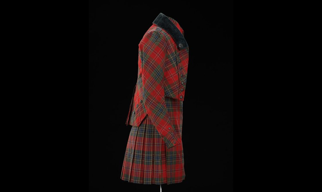A side view of a mannequin wearing a red tartan kilt with a matching jacket.