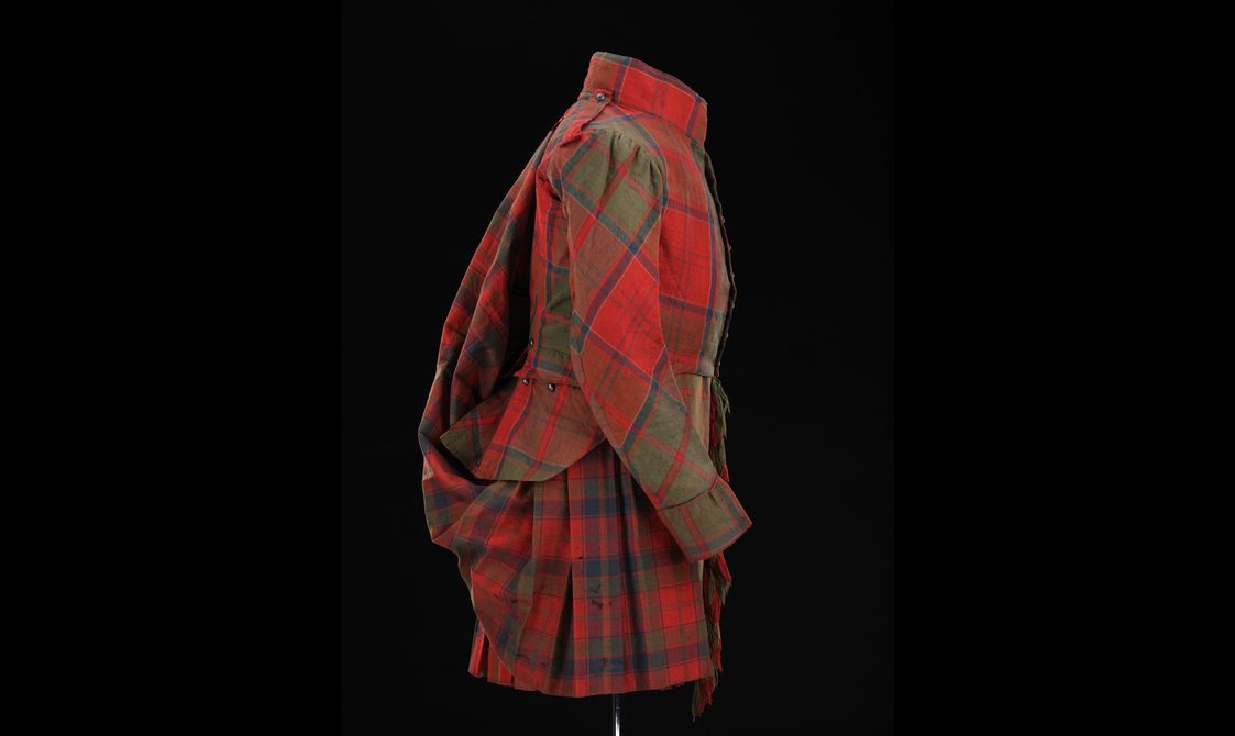 Side view of a mannequin wearing a red tartan kilt with a matching jacket with pinned up coat tails.