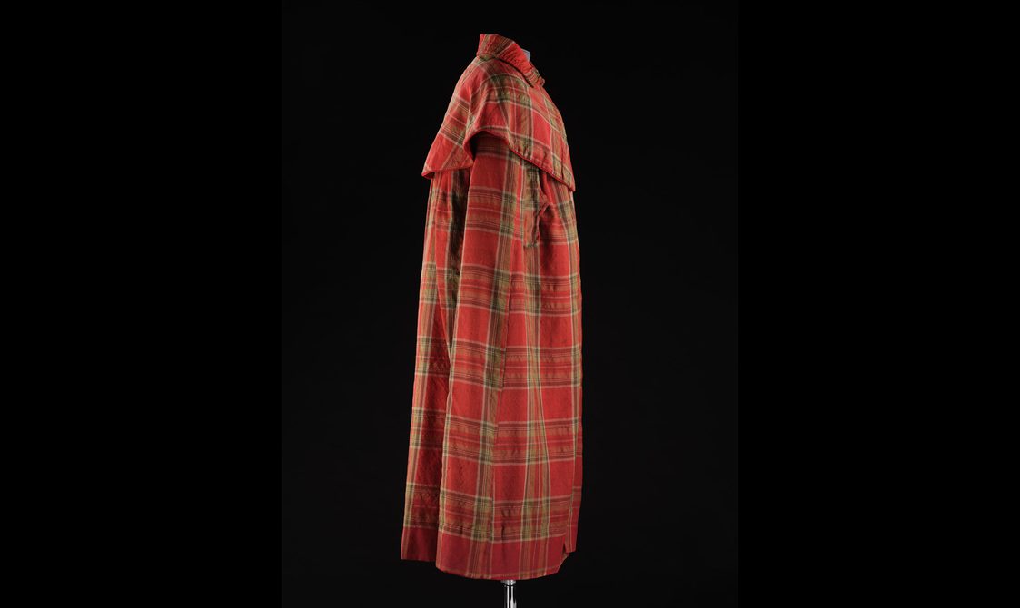 A side view of a mannequin wearing a long red tartan cloak