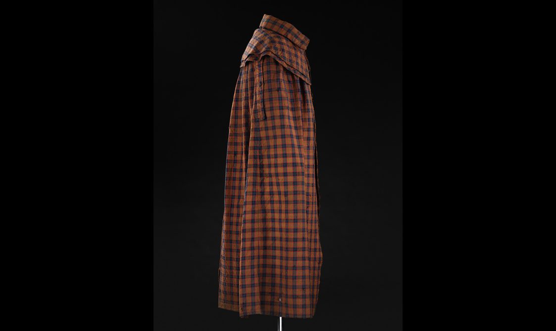 Side view of a mannequin wearing a brown, navy, and red tartan cloak