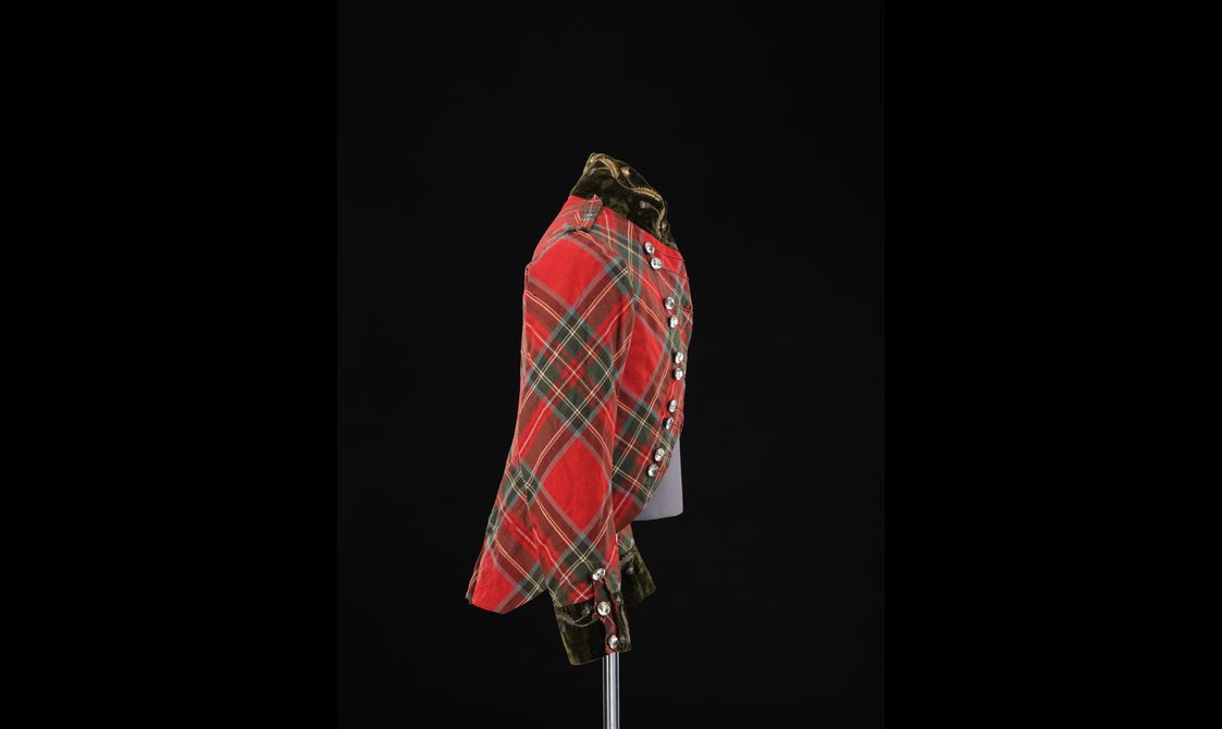 Side view of a mannequin wearing a short red tartan jacket with a velvet collar and cut glass buttons.