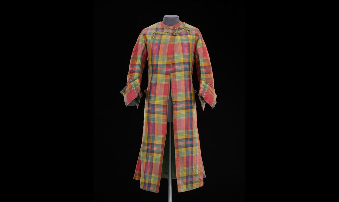 A mannequin wearing a long red, green, and yellow tartan silk coat with large cuffs.