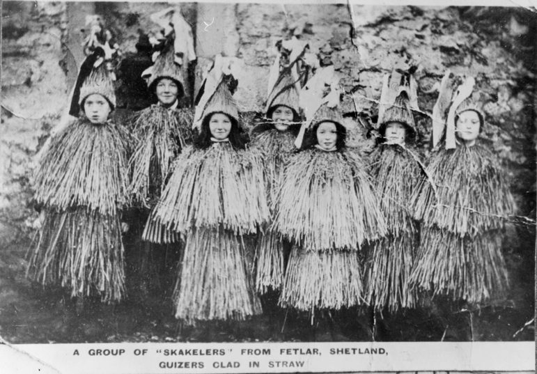 A black and white photograph of women dressed in tall coned decorative hats and flowing, straw like tops and skirts.