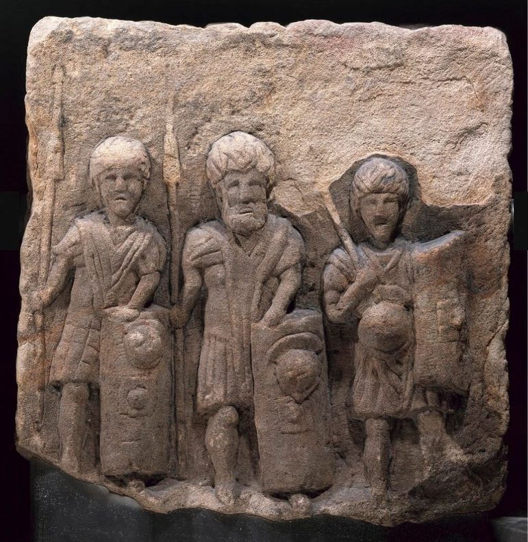 A slab of rock with three Roman army soldiers holding spears and shields carved into its surface.