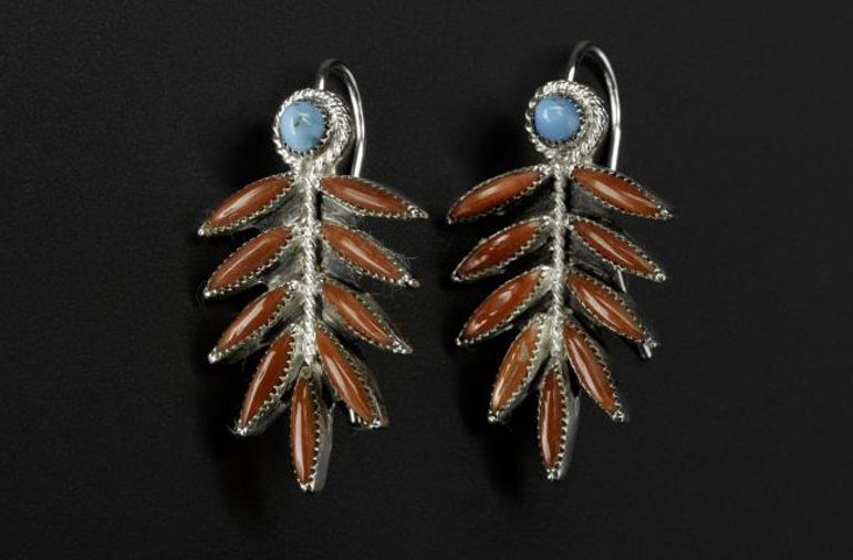 A pair of long silver earrings with turquoise circles and coral leaf like shapes photographed against a black background
