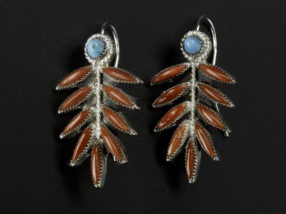 A pair of long silver earrings with turquoise circles and coral leaf like shapes photographed against a black background