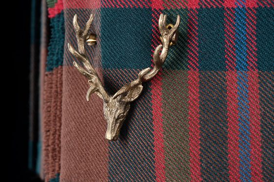 A detail of a red, green, and blue tartan kilt with a pin of a stag head.