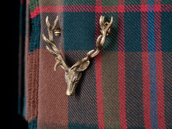A detail of a red, green, and blue tartan kilt with a pin of a stag head.