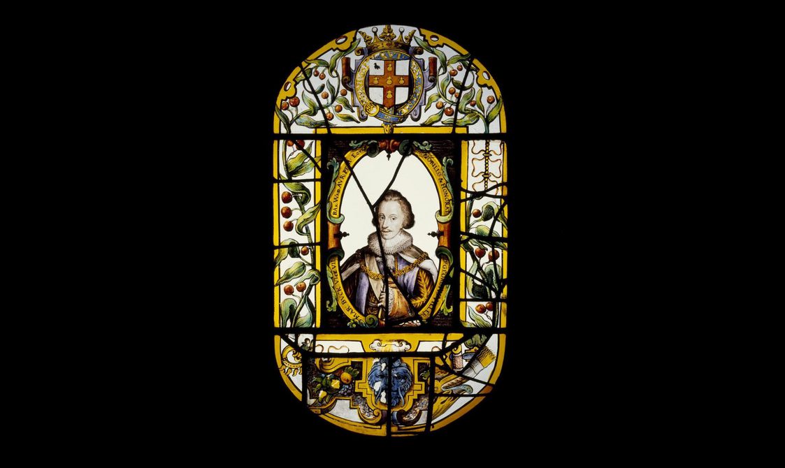 An elaborate stained glass window of a king wearing a ruffled collar and black feathered hat. He is surrounded by flowers, royal crests, and text.