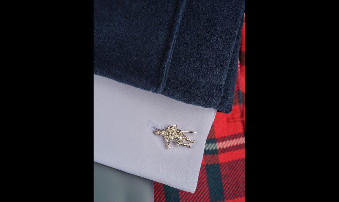 Detail of a white shirt with a silver cufflink of a Highland warrior figure.