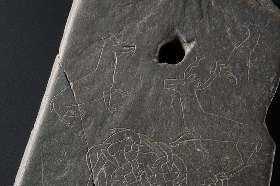 Grey stone with a small hole near the top and intricate carving of two deer.