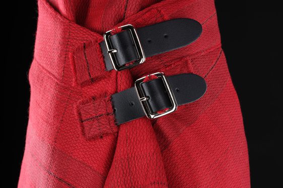 A detail of a red kilt with a subtle grid pattern with two leather buckles fastening the side.