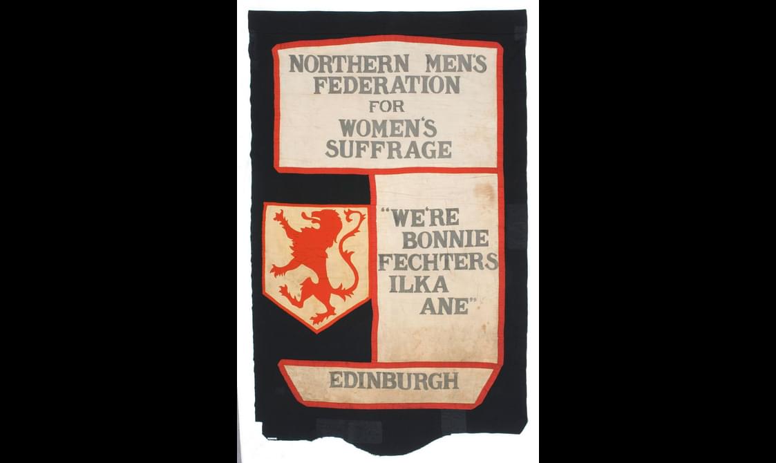 A banner with slogans and a red lion. The slogans read, "Northern Men's Federation for Women's Suffrage. We're bonnie fechters ilka ane. Edinburgh."