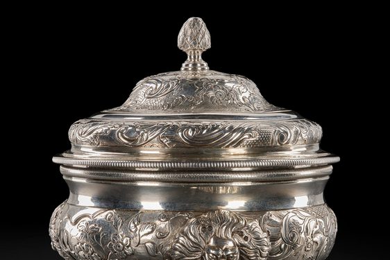 An ornate silver sugar bowl with three short legs and a lid